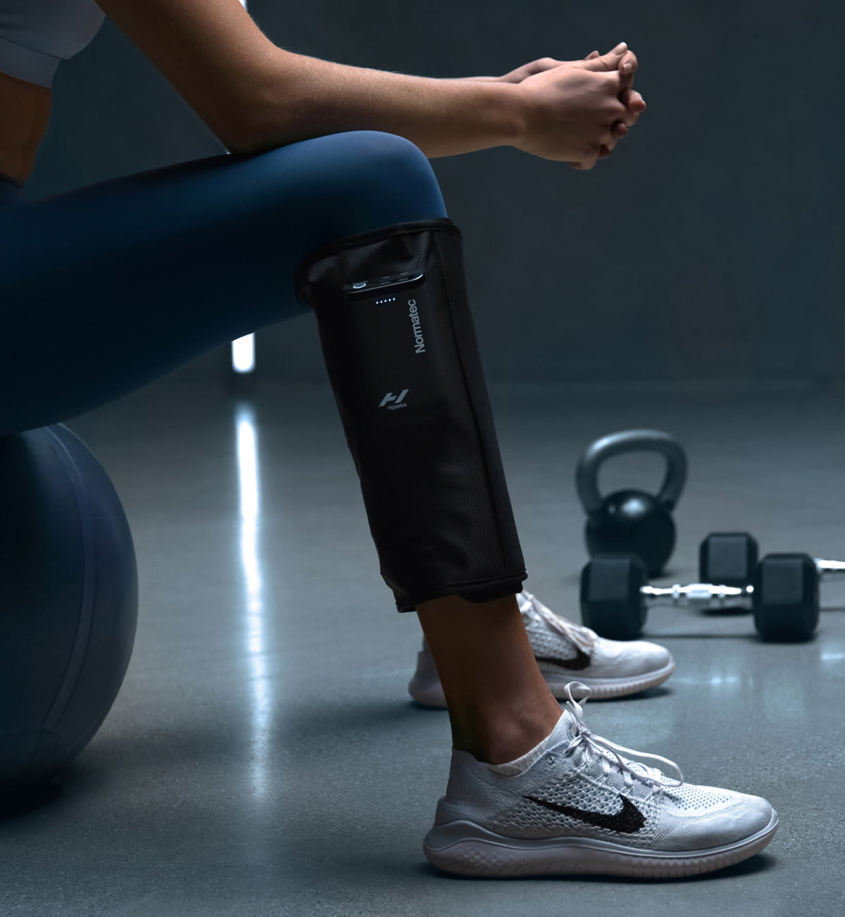 Person sitting in a gym wearing Normatec Lower Legs
